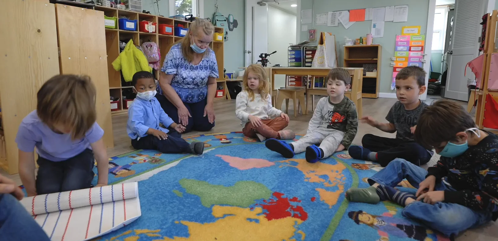 Adult and children gathered on a classroom rug in school-supplied footage