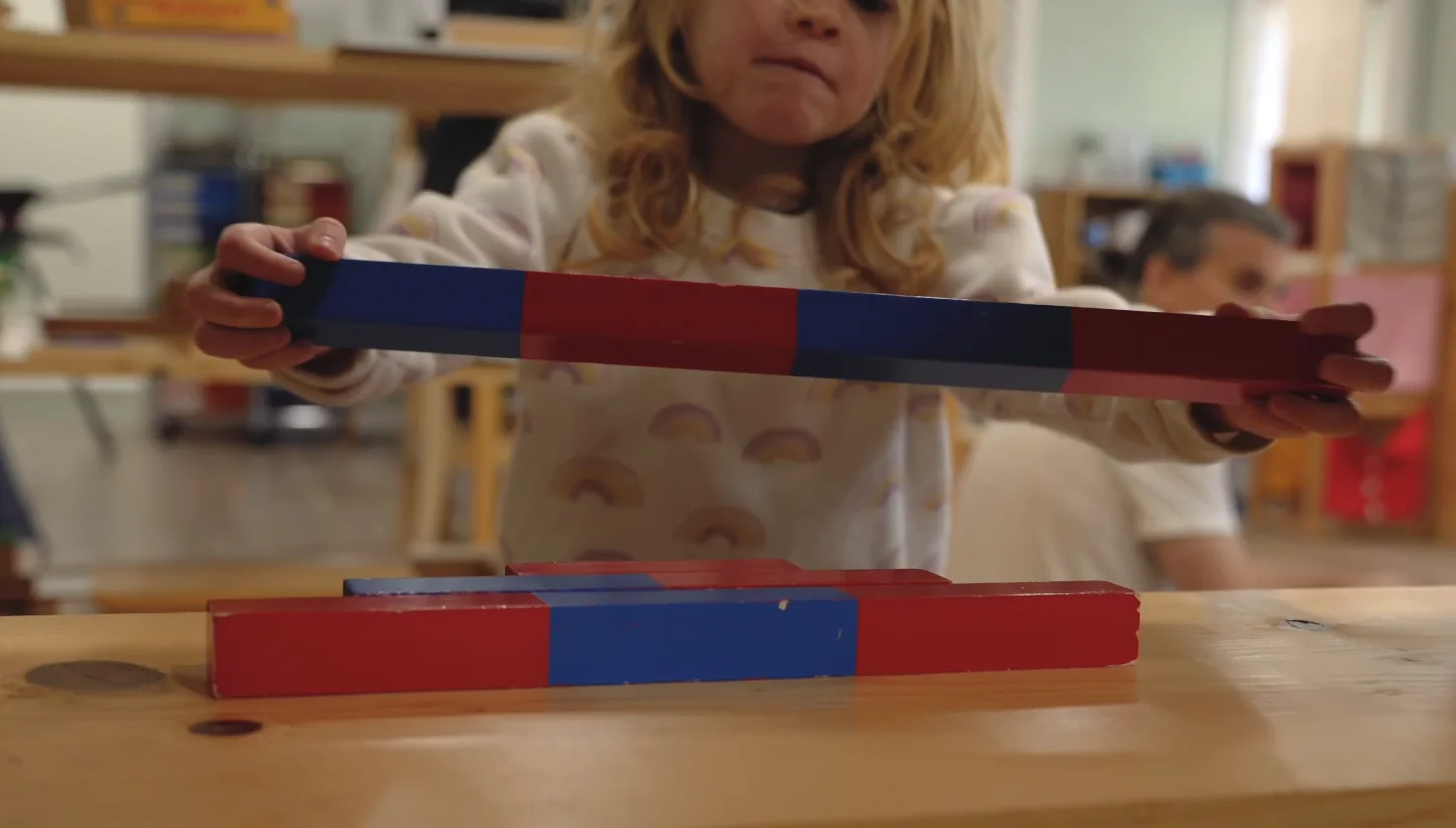 Child working with red and blue number rods in school-supplied footage